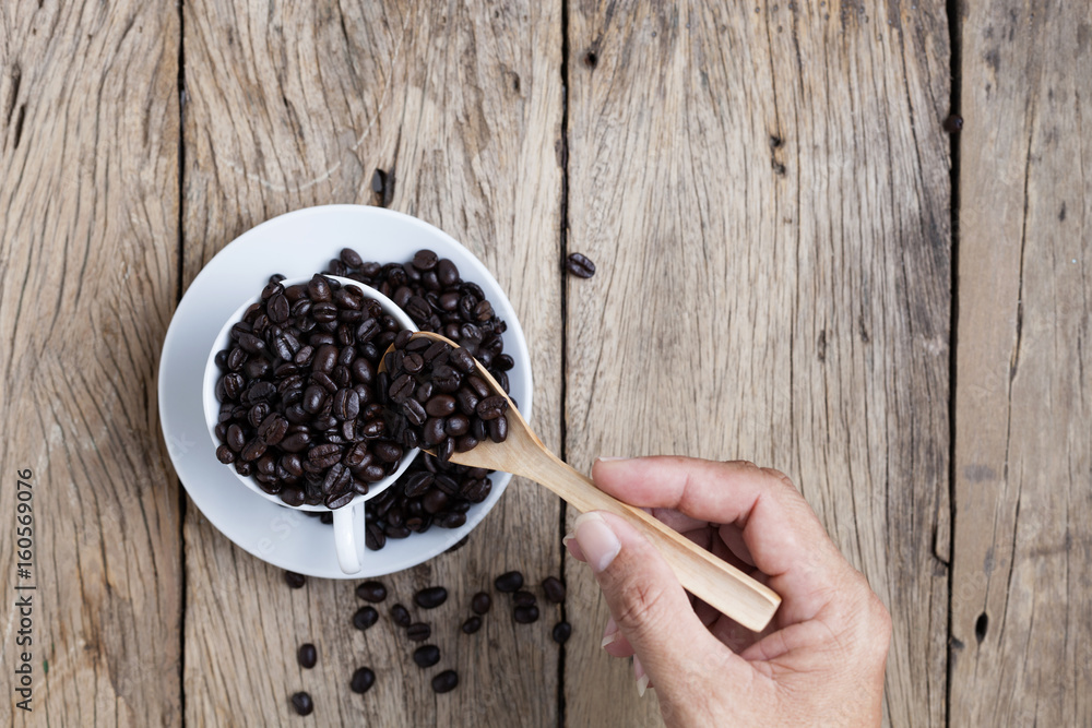 hand holding wooden spoon with coffee beans in the white coffee cup.