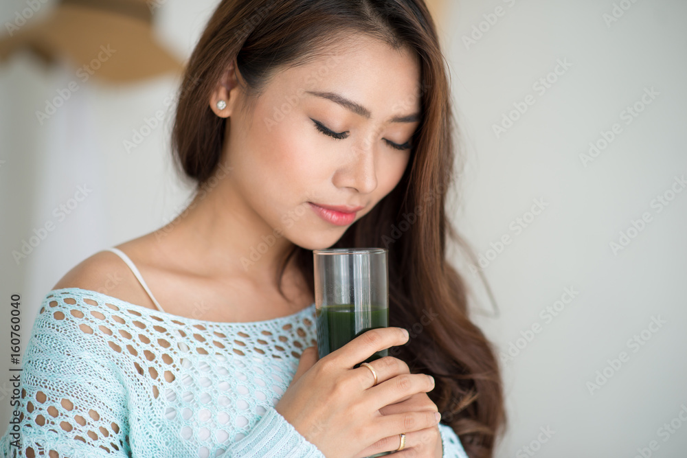 漂亮的年轻亚洲女人在家喝绿色新鲜蔬菜汁或冰沙