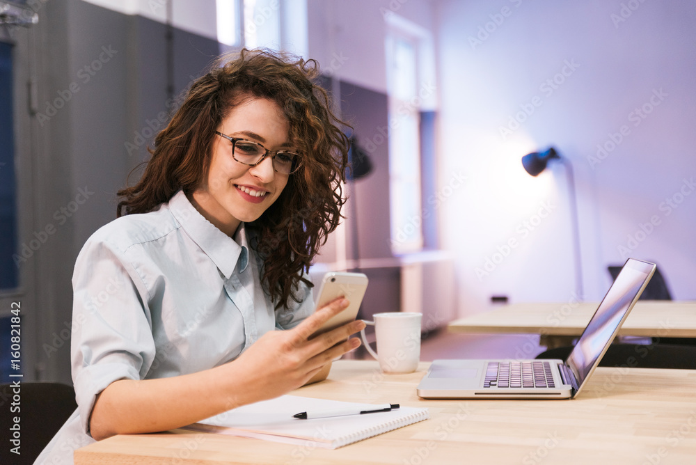 Curly girl wearing glasses smiling while looking at her phone