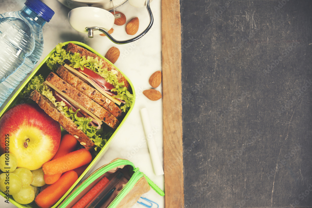 Sandwich, apple, grape, carrot, stationery and bottle of water on white wooden background.