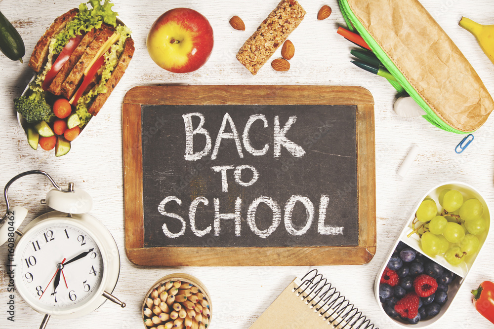 Sandwich, apple, grape, carrot, berry in plastic lunch boxes, stationery and bottle of water