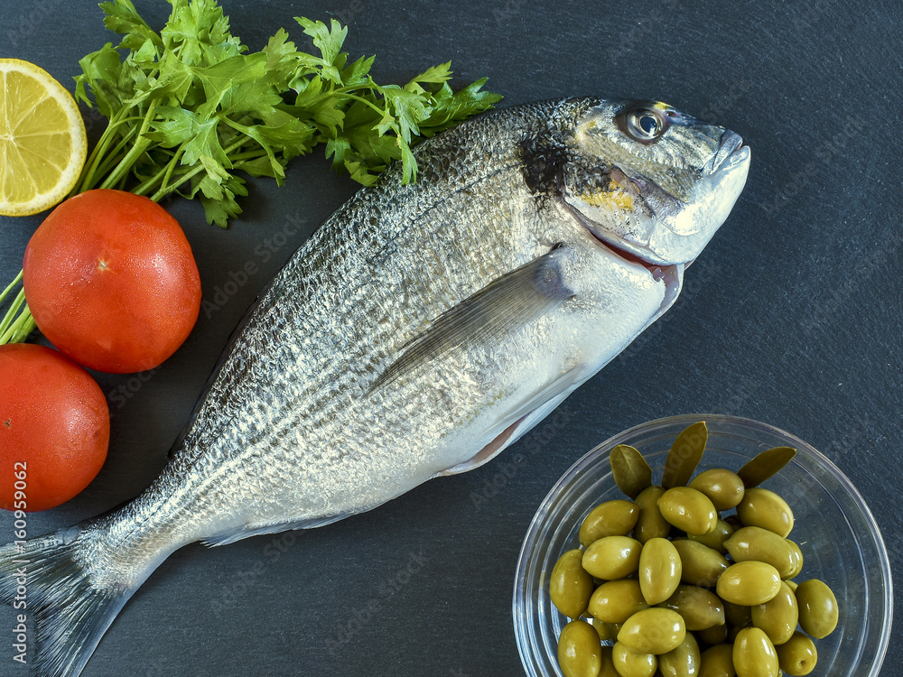 One ready to cook raw bream fish with vegetables on stone slate board.