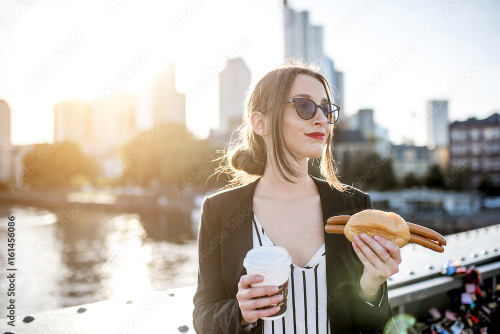 年轻的女商人在带s的桥上吃着传统的法兰克福香肠和咖啡