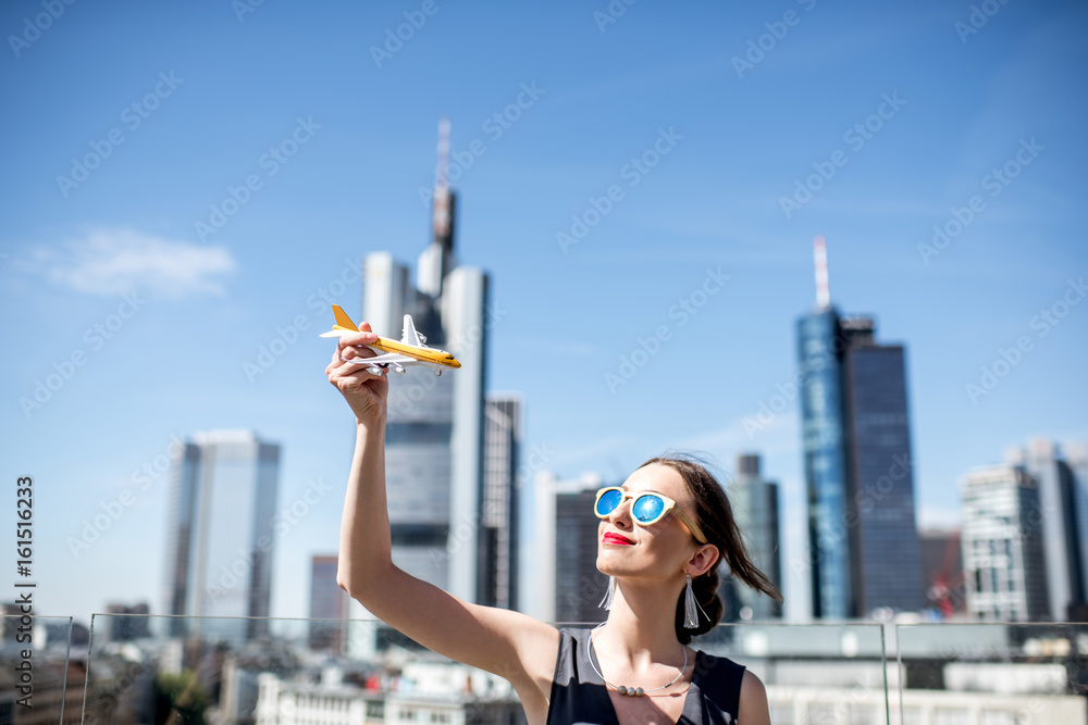 Young woman playing with toy airplane on the modern cityscape background in Frankfurt. Air transport