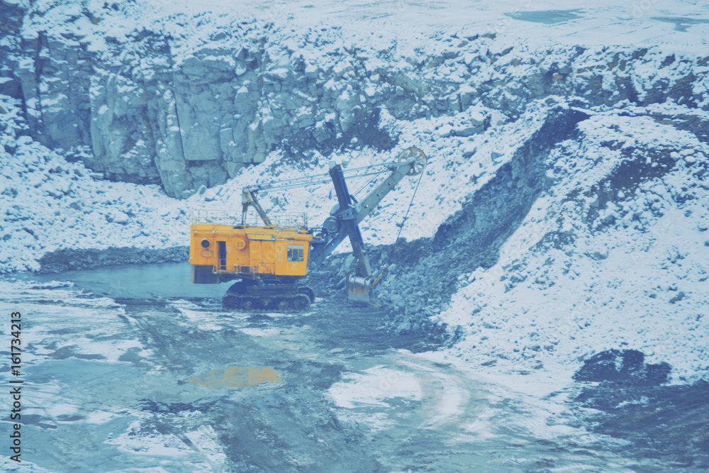 big huge yellow excavator in a granite quarry in winter. huge loading shovel bucket stands on a gran