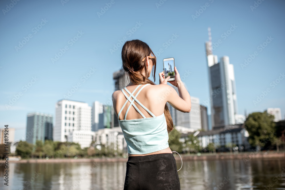 穿着运动服的年轻女子用手机拍摄弗兰克现代街区美丽的天际线