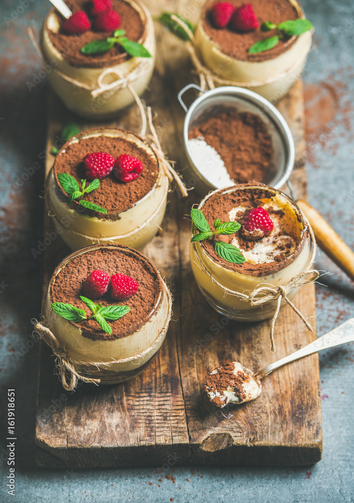 Homemade Italian dessert Tiramisu in individual glasses with mint leaves, fresh ripe raspberries and