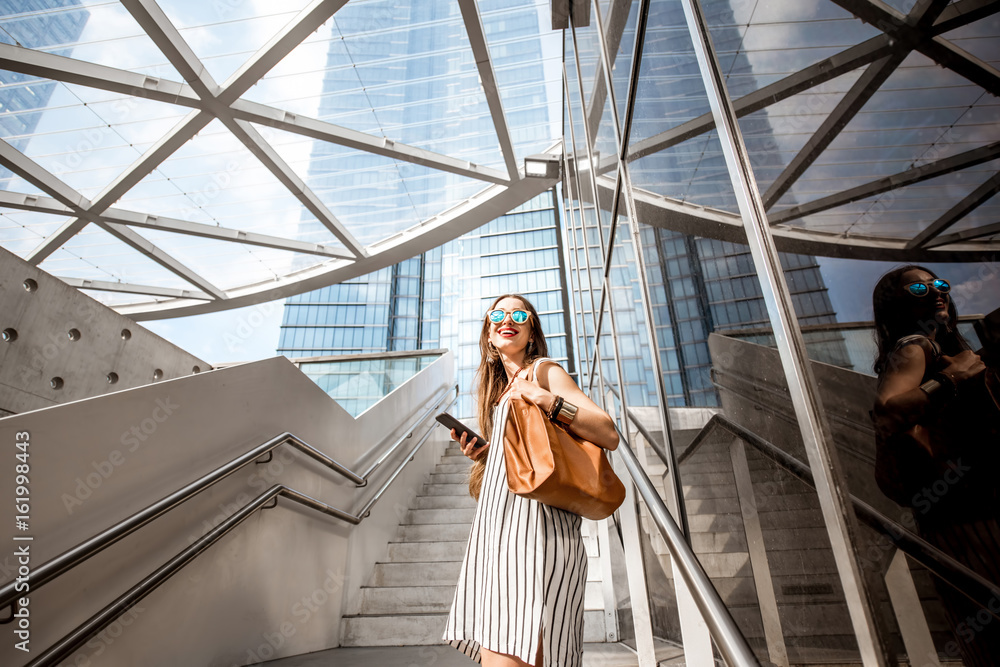 年轻漂亮的女商人拿着电话站在户外现代办公室附近的楼梯上