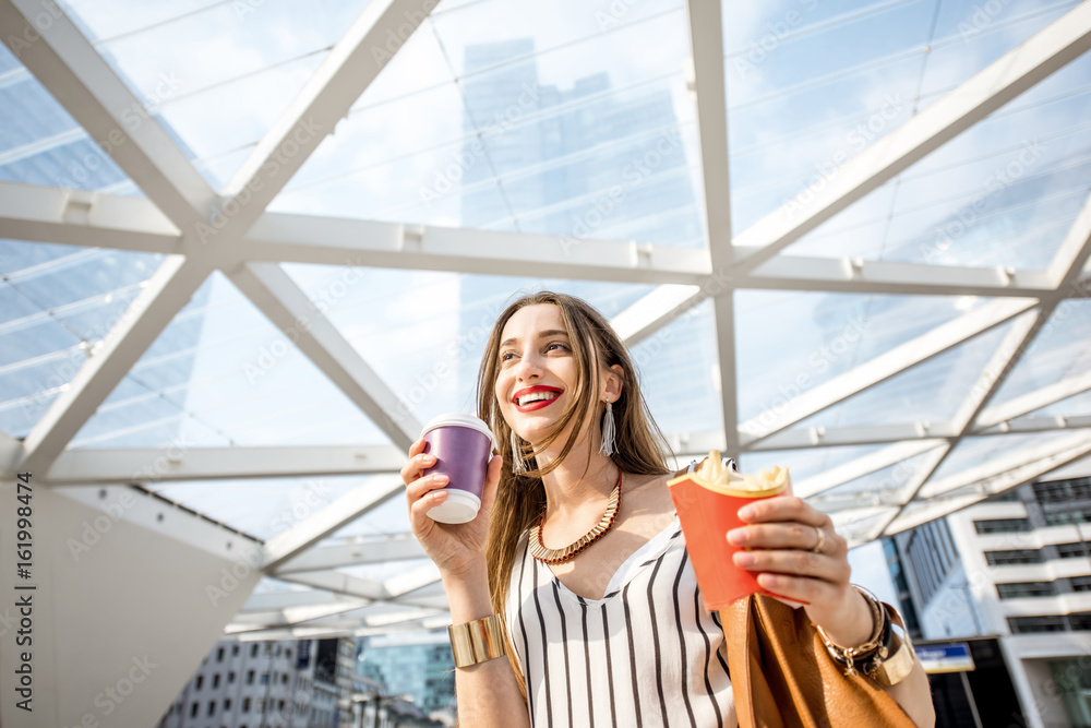 年轻的女商人在现代办公室附近的户外吃快餐，配薯条和咖啡