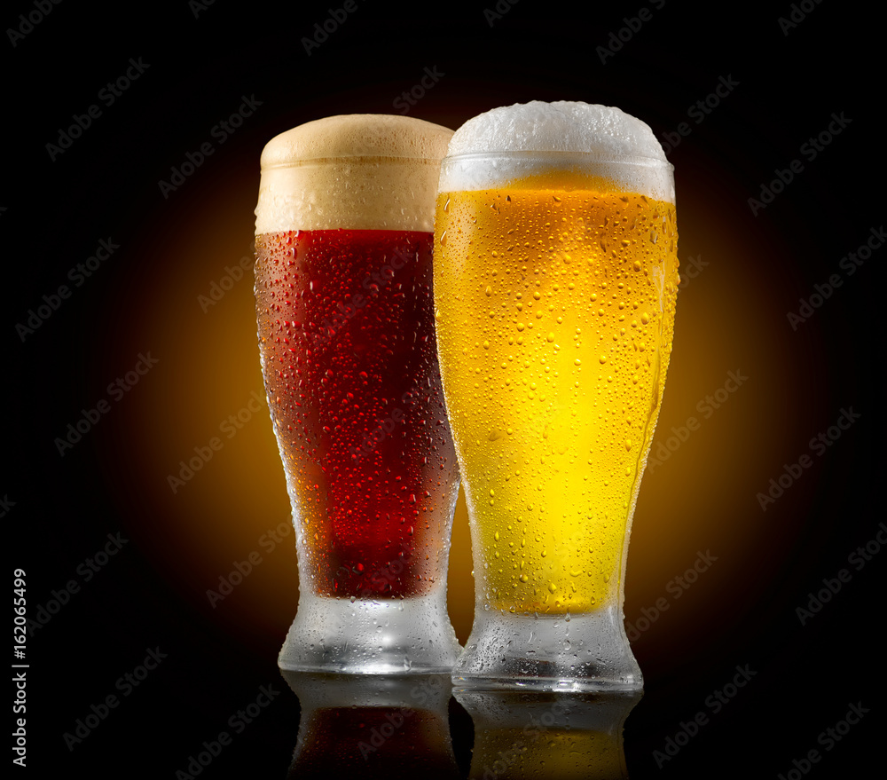 Craft beer. Two glasses of cold light and dark beer isolated on black background