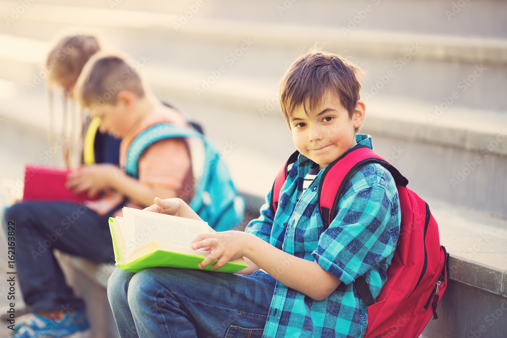 Children with rucksacks sitting on the stairs near school. Pupils with books and backpacks outdoors