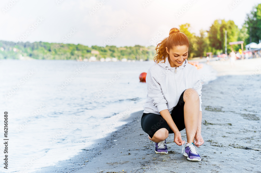 Woman tying laces before training on beach.