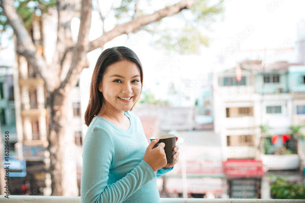 一个快乐的亚洲女人在早餐时拿着咖啡或茶杯思考的画像