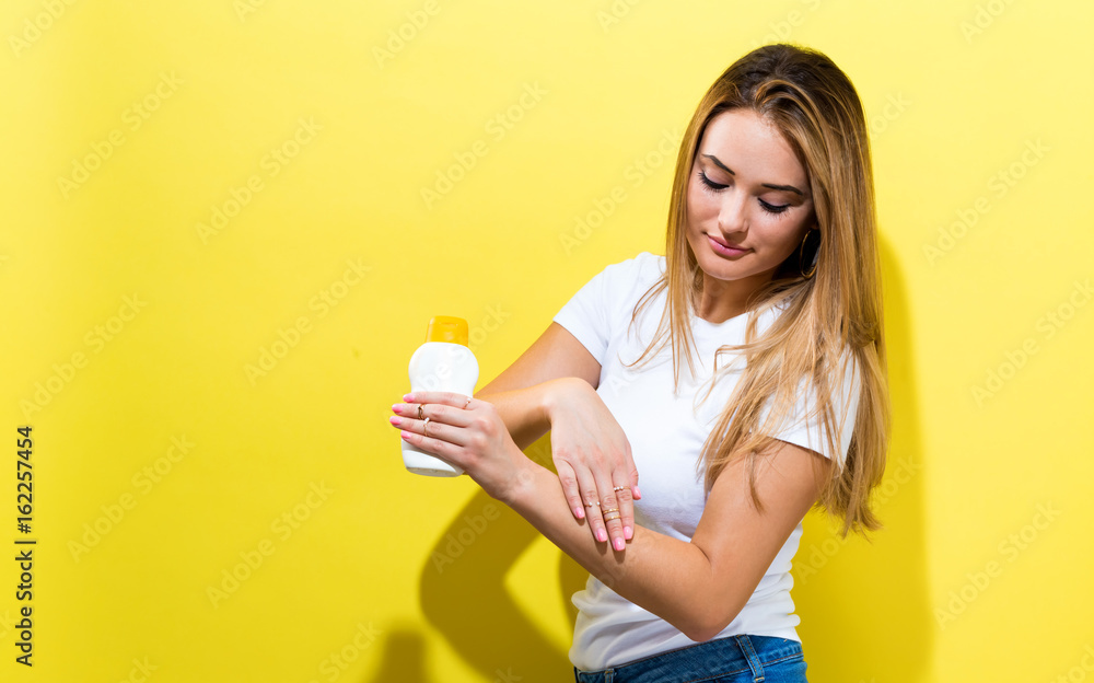 Young woman a bottle of sunblock on a yellow background