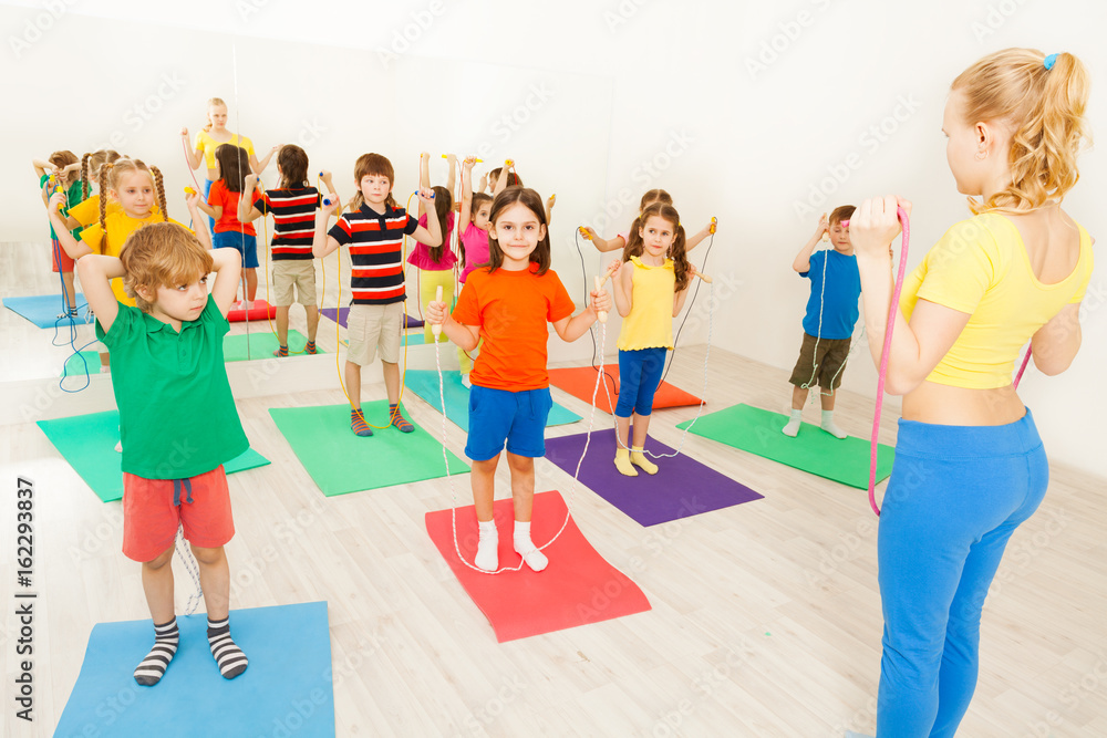 Happy kids exercising with jumping rope in gym