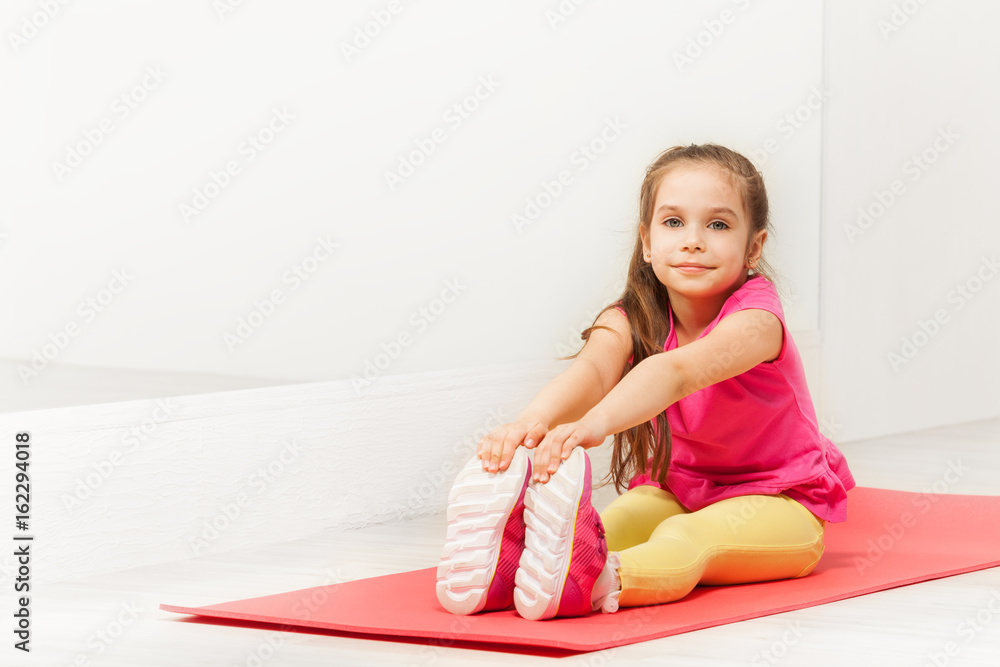 Young gymnast sitting on mat and stretching legs