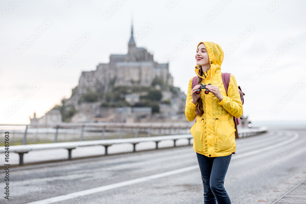 穿着黄色雨衣的年轻女旅行者在前往法国著名圣米歇尔岛的路上