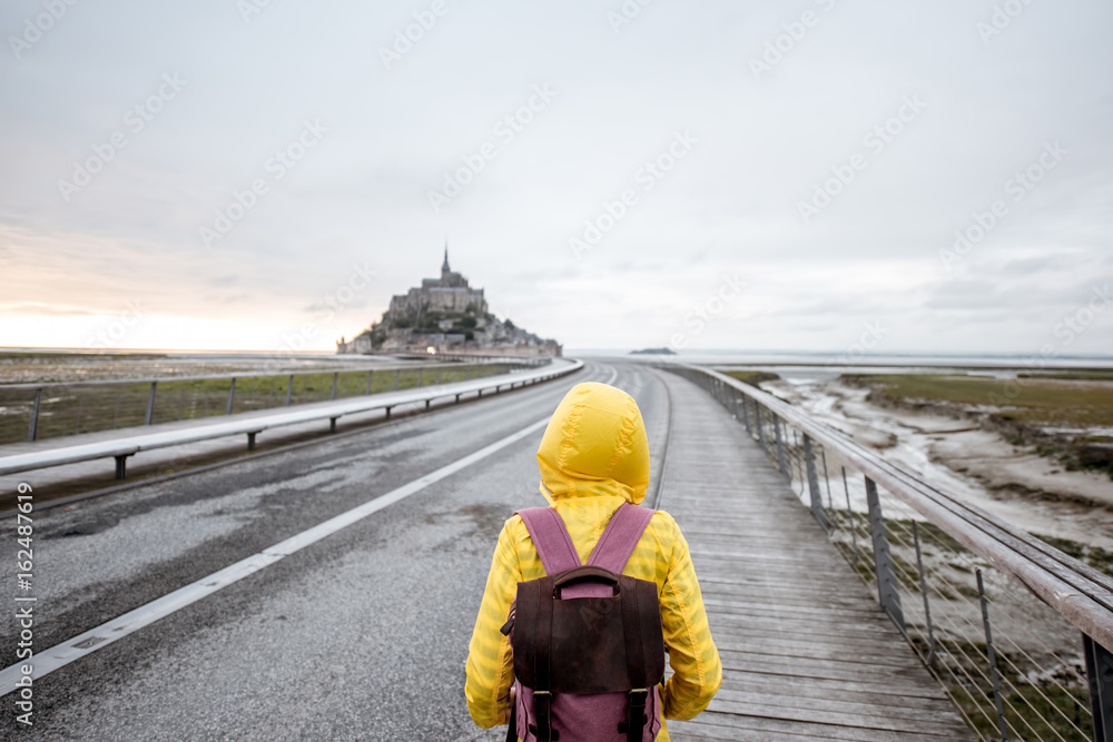 穿着黄色雨衣的年轻女旅行者在前往法国著名圣米歇尔岛的路上