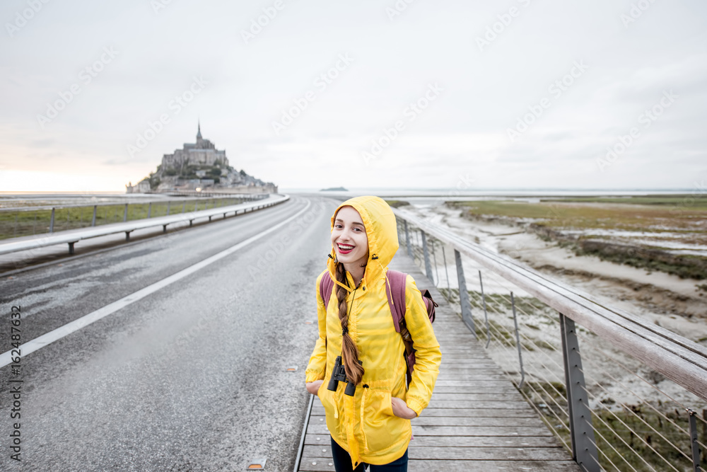 Young female traveler in yellow raincoat on the road to famous saint Michel island in France