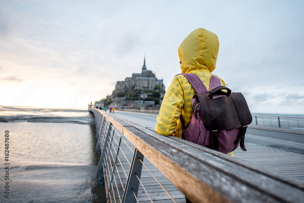 Young female traveler in yellow raincoat on the road to famous saint Michel island in France