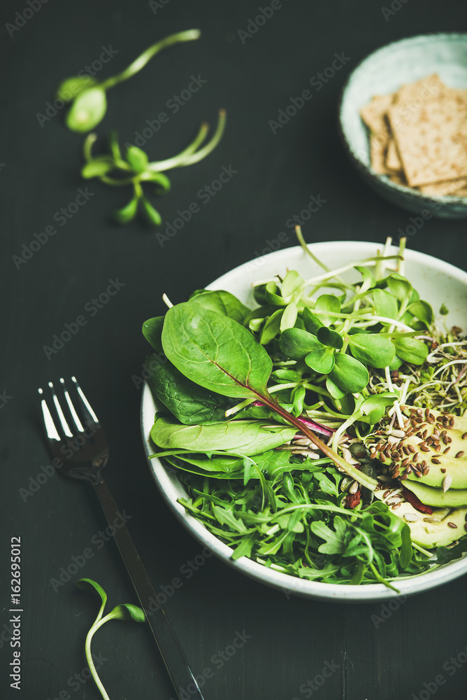 Green vegan breakfast meal in bowl with spinach, arugula, avocado, seeds and sprouts over black back