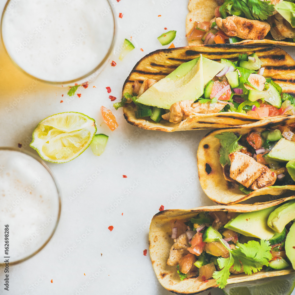 Healthy corn tortillas with grilled chicken fillet, avocado, fresh salsa, limes, beer over light gre