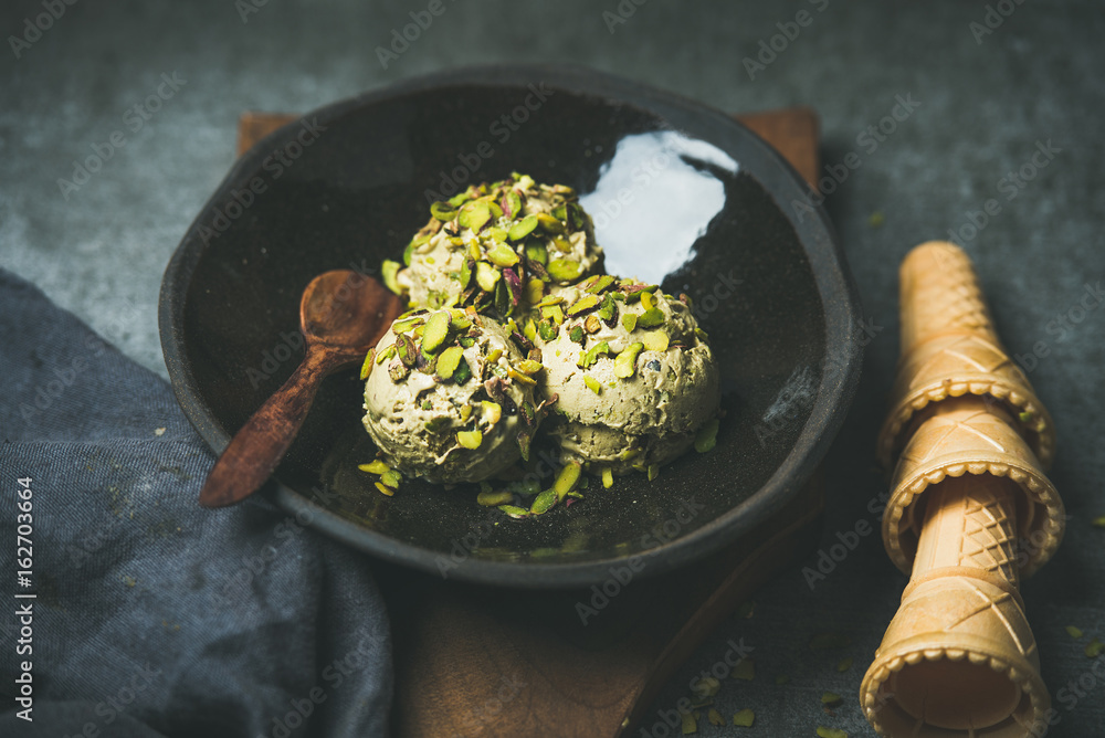 Homemade pistachio ice cream scoops with crashed pistachio nuts in dark plate over wooden board, waf