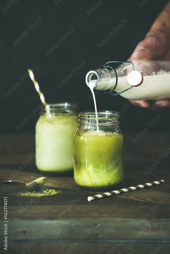 Cold refreshing summer iced coconut matcha latte drink, hand pouring milk over glass. Selective focu