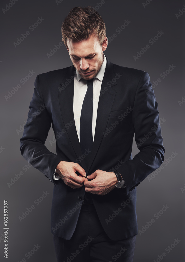 Stylish businessman in a suit standing aganst a grey background