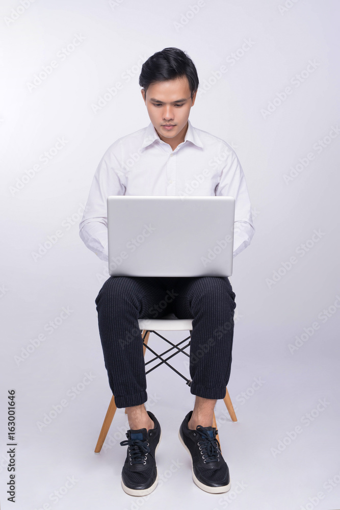 Smart casual asian man seated on chair, using laptop in studio background