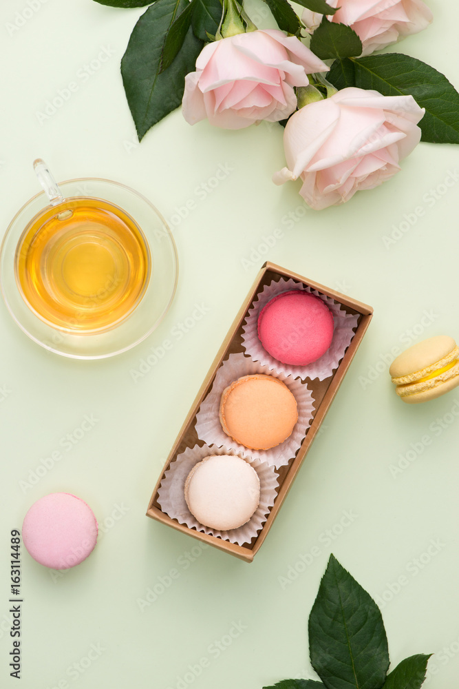 French macaroons. Many variegated sweet macarons in box with bouquet of pink roses on the table