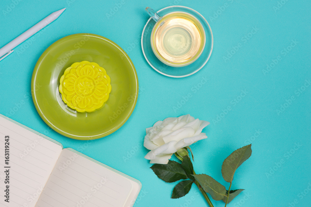 Snow skin mooncake and tea cup with flowers on dark background. Open notebook with copy-space.