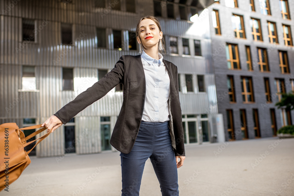 Lifestyle portrait of a young businesswoman swinging bag outdoors at the modern residential district