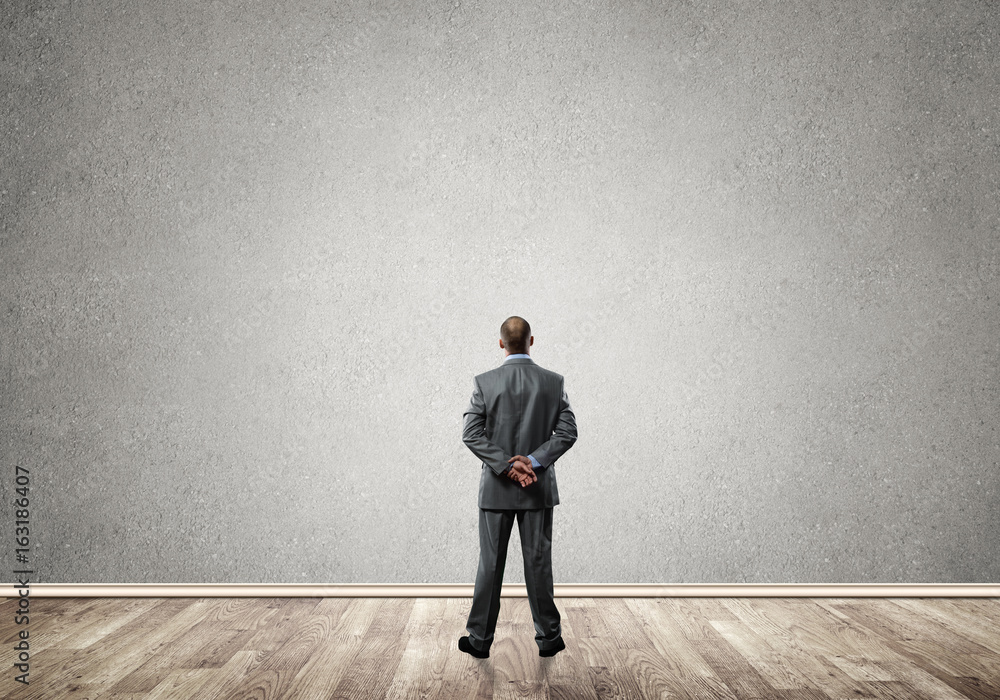 Businessman with hands behind his back and looking at blank concrete wall