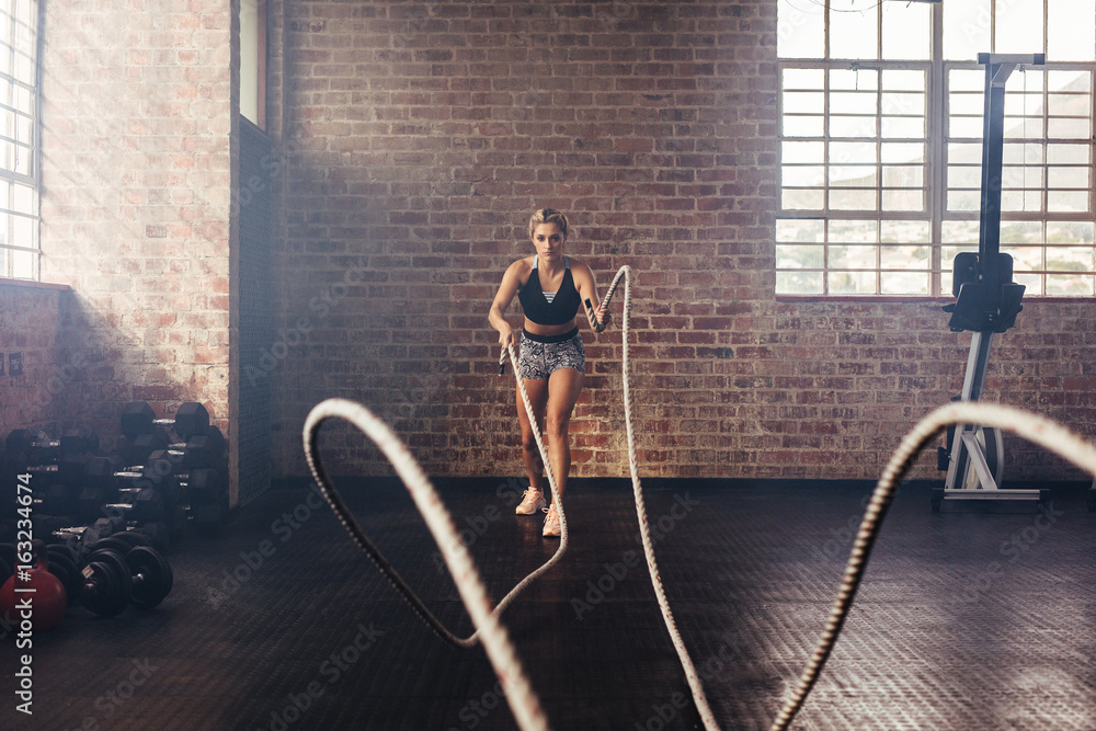 Athlete exercising in gym using heavy ropes.