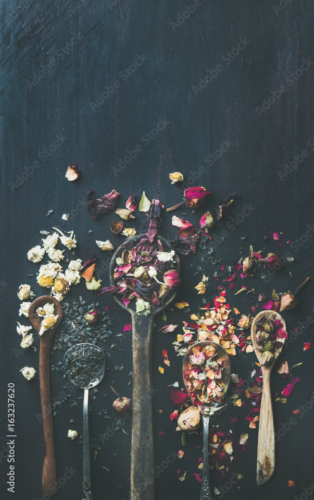 Wooden spoons with dry herbs, flower buds and tea leaves over black scorched wooden background, top 