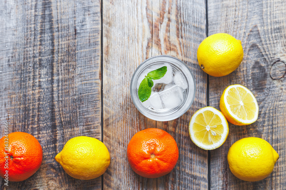 glass with ice and lemons, oranges, mint on wooden table