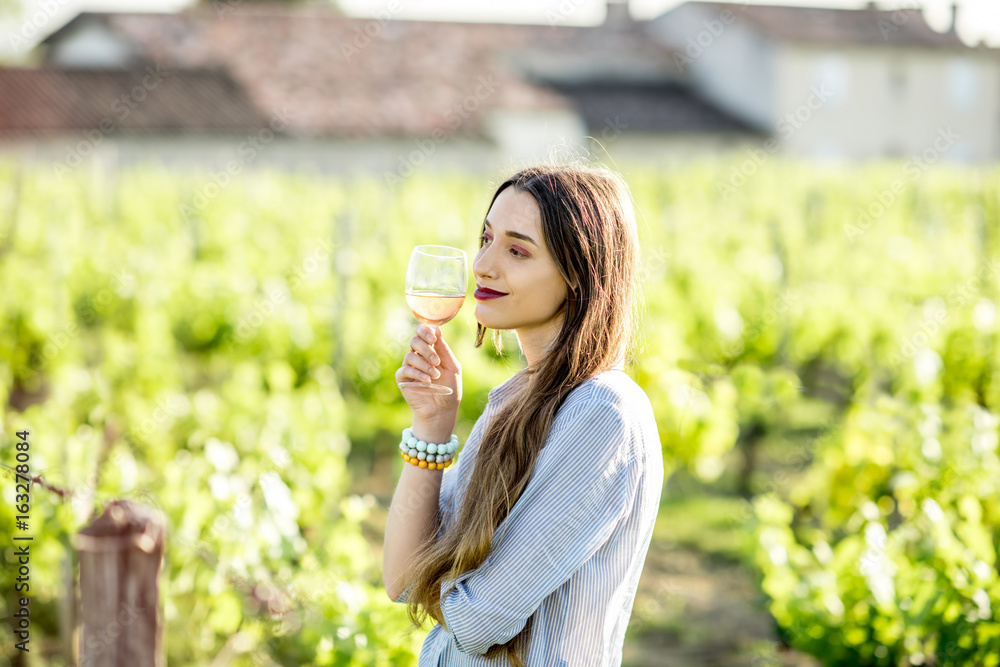 Young woman tasting wine standing outdoors on the vineyard in Bordeaux region during the sunset in F