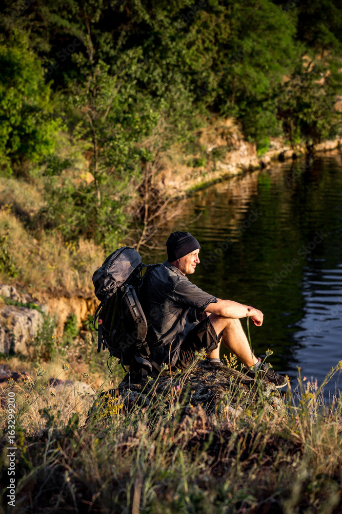 Young tourist with backpack standing on a rock and enjoying sunset