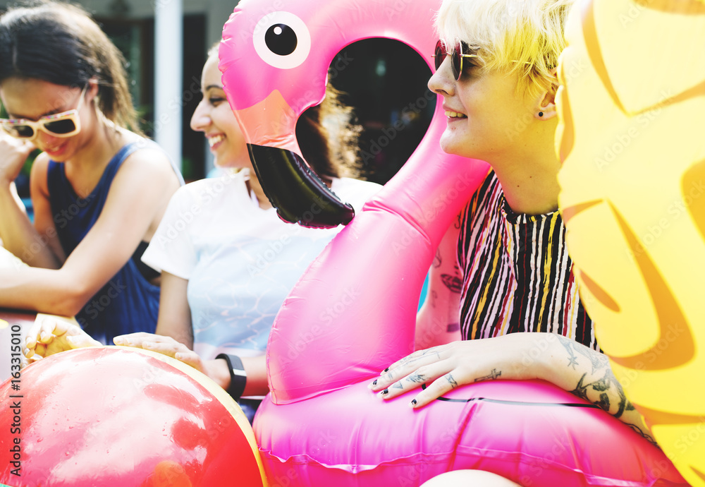 Group of diverse women sitting by the pool with inflatable tubes