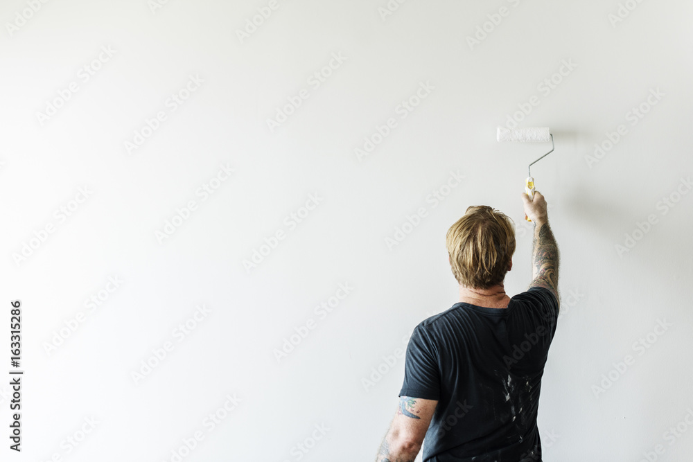 Man with tattoo holding roller paint the wall