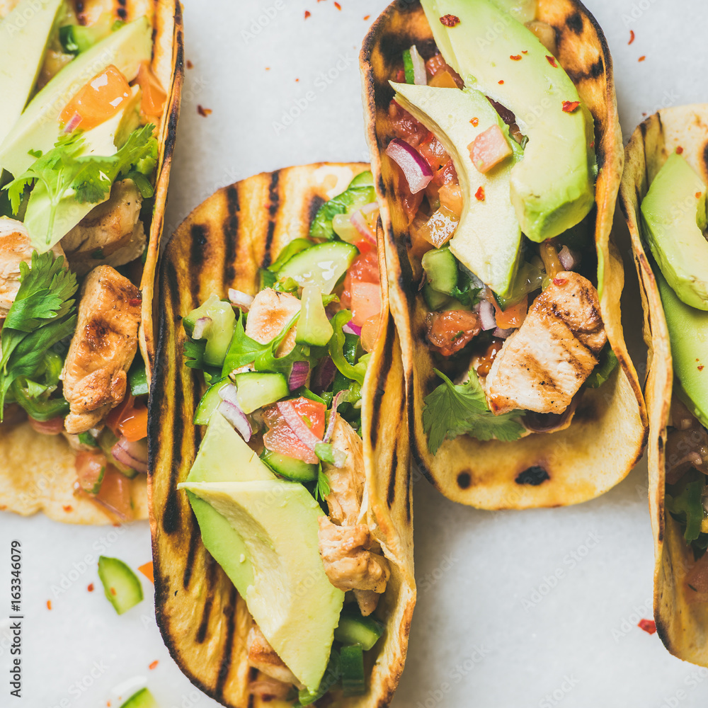 Healthy corn tortillas with grilled chicken fillet, avocado, fresh salsa, limes over light grey marb