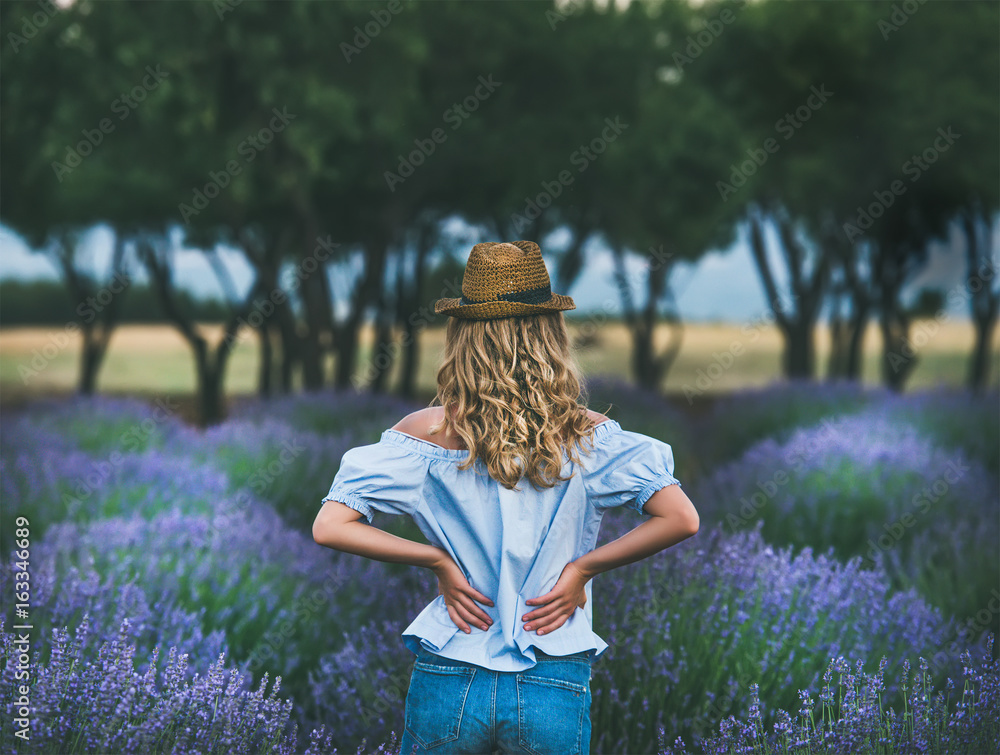 Young blond woman traveller wearing straw hat, denim shorts and blue off-shoulder blouse standing in