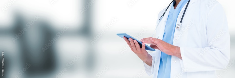 Doctor mid section holding tablet against blurry grey office