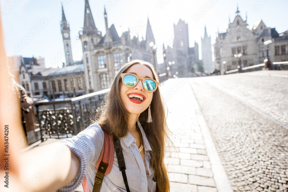 Young woman tourist making selfie photo standing on the bridge with beautiful view on Gent city in B