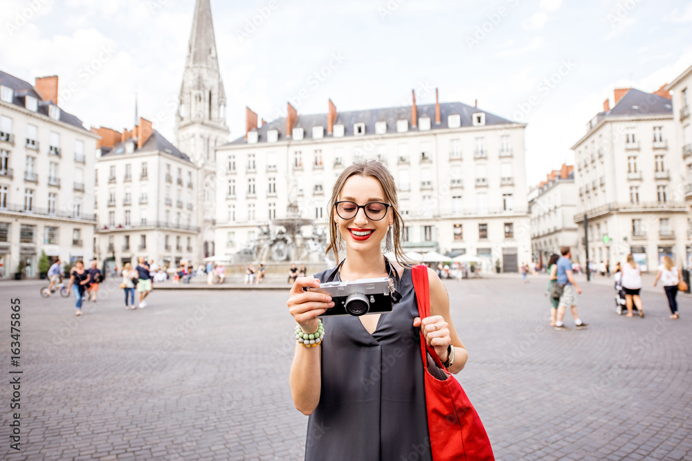 Young woman tourist with photo camera and red bag walking on the Royal main square in Nantes city, F