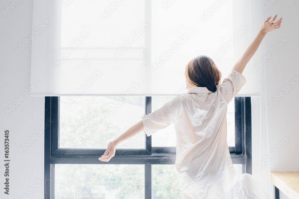 Asian woman stretching near the window after her wake up in the morning, back view.