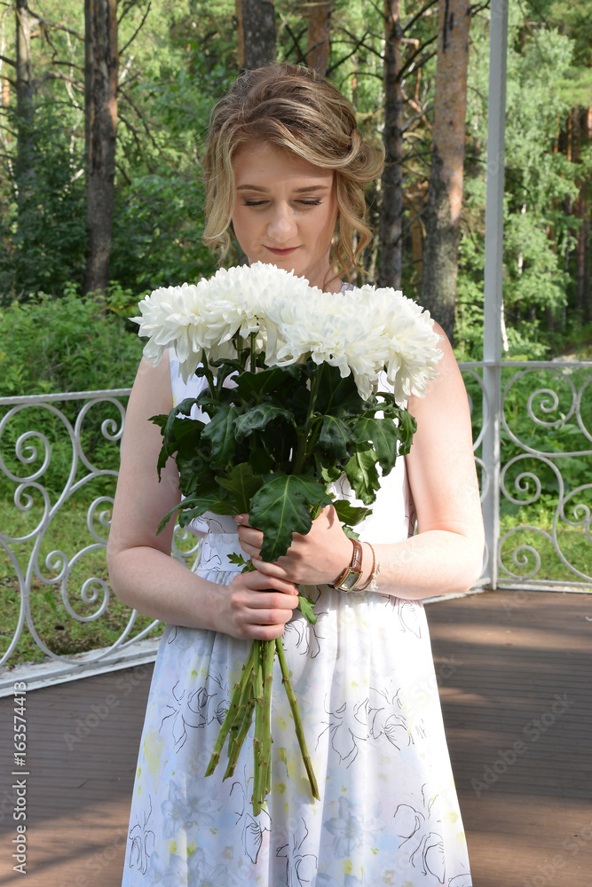 A happy girl in a long dress with flowers is standing in a forest arbor.