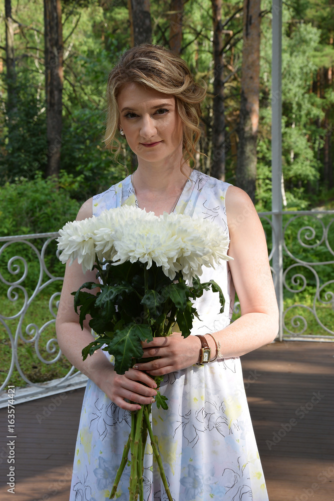 A happy girl in a long dress with flowers is standing in a forest arbor.