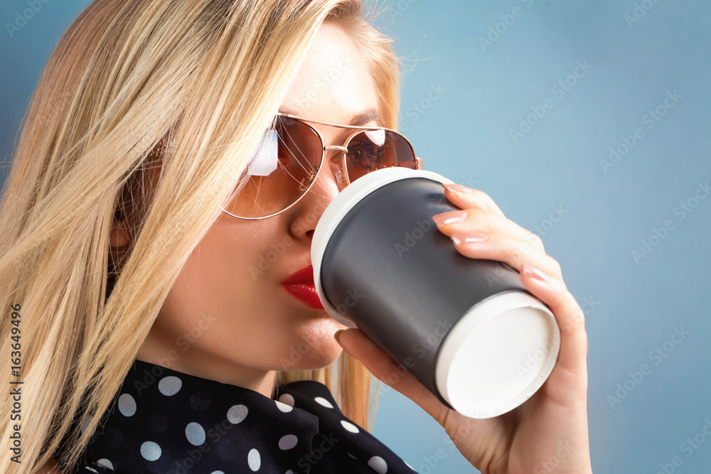  Happy young woman drinking coffee on a gray background